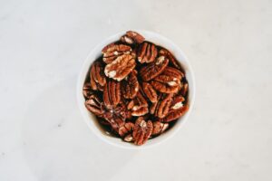 A bowl of pecans with shelled pecan halves on a wooden table