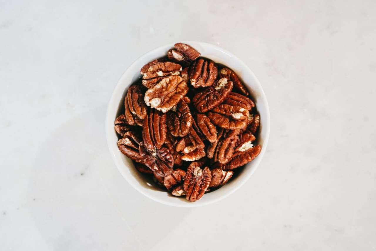 A bowl of pecans with shelled pecan halves on a wooden table